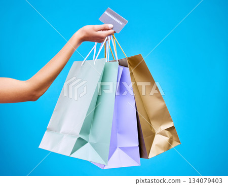 Woman, hands and shopping bags with credit card for purchase, sale or discount against a blue studio background. Hand of female shopper holding gift bag or presents for banking transaction or buying Woman, hands and shopping bags with credit card for purchase, sale or discount against a blue studio background. Hand of female shopper holding gift bag or presents for banking transaction or buying 134079403