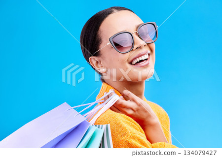 Shopping bags, retail and woman portrait with a smile and sunglasses from boutique sale. Happy, customer and female model with store bag and sales choice in isolated blue background in studio 134079427