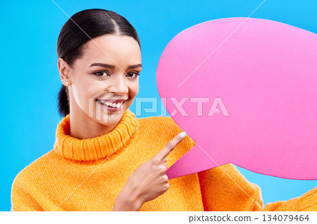 Speech bubble, happy and portrait of woman pointing to banner in studio for advertising on blue background. Face, smile and girl with poster, mockup and space for social media, announcement or news 134079464