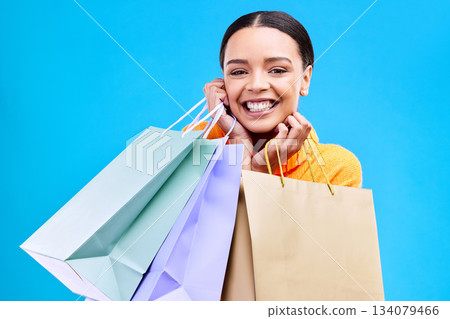Shopping bags, excited and woman portrait with a smile and happiness from boutique sale. Happy, customer and female model with store bag and sales choice in isolated blue background and studio 134079466