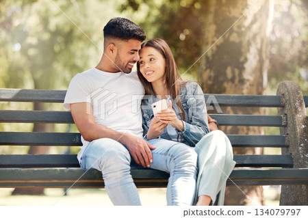 Happy couple, phone and relaxing on park bench together browsing social media and bonding in nature. Man and woman smile in happiness for relationship on mobile smartphone in the summer outdoors Happy couple, phone and relaxing on park bench together browsing social media and bonding in nature. Man and woman smile in happiness for relationship on mobile smartphone in the summer outdoors 134079797