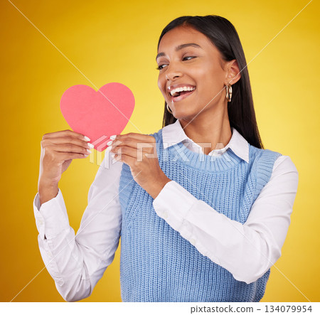 Happy, paper and heart with woman in studio for love, support and romance. Valentines day, kindness and date with female and holding symbol on yellow background for health, happiness and hope Happy, paper and heart with woman in studio for love, support and romance. Valentines day, kindness and date with female and holding symbol on yellow background for health, happiness and hope 134079954