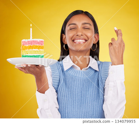 Smile, wish and woman with cake in studio for happy celebration or party on yellow background. Happiness, excited gen z model with fingers crossed and candle in rainbow dessert to celebrate milestone Smile, wish and woman with cake in studio for happy celebration or party on yellow background. Happiness, excited gen z model with fingers crossed and candle in rainbow dessert to celebrate milestone 134079955