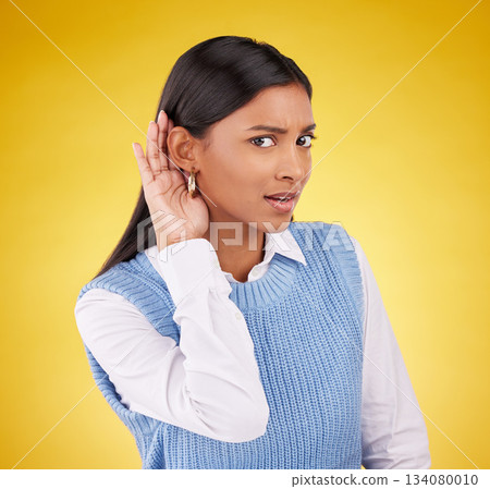 Portrait, confused and gossip with a woman on a yellow background in studio listening to a secret. Hand gesture, doubt and shock with an attractive young female cupping her ear to hear a rumor 134080010
