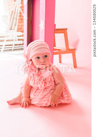 Moscow, Russia, 29.06.23. A baby girl is sitting on the floor wearing a pink dress and a pink hat 134080029
