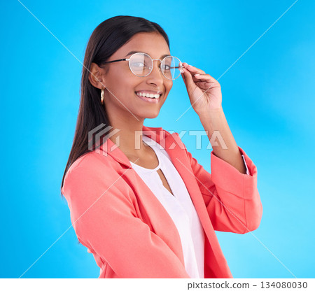 Woman, glasses and happy portrait in studio with a smile for eye care and vision with frame or lens. Smile of Indian female model person on a blue background with specs for fashion and business 134080030