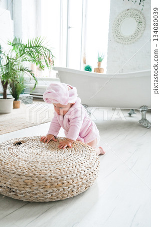 Moscow, Russia, 29.06.23. A baby in a pink robe is playing on a round rug Moscow, Russia, 29.06.23. A baby in a pink robe is playing on a round rug 134080039
