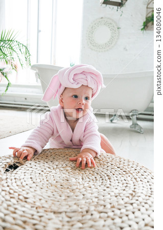 Moscow, Russia, 29.06.23. A baby wearing a pink towel and a pink robe is laying on a rug Moscow, Russia, 29.06.23. A baby wearing a pink towel and a pink robe is laying on a rug 134080046
