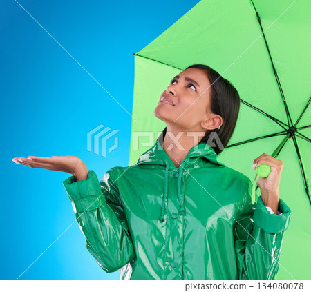 Sad, looking and a woman with an umbrella for the rain isolated on a blue background in a studio. Confused, insurance and a girl waiting for bad weather, disappointed and feeling for water in winter 134080078