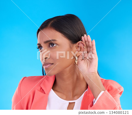 Listening, secret and gossip with a woman on a blue background in studio cupping her ear for hearing. Privacy, whisper and hand gesture with an attractive young female trying to hear news or a rumor 134080121