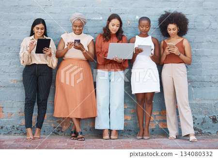 Technology, diversity and business women by a wall standing in a line doing research online. Professional females with phone, tablet and laptop working on a resume while waiting for a job interview. 134080332