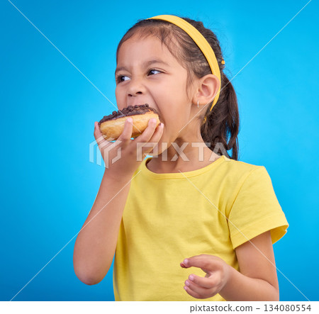 Donut, eating and sweet with girl in studio for junk food, sugar and happiness. Snack, cake and cute with face of child and dessert for candy diet and chocolate isolated on blue background 134080554
