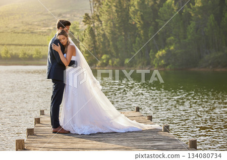 Wedding couple, hug and love by lake in nature for relax or romantic honeymoon getaway. Calm woman hugging man in happy marriage relaxing by water together enjoying the loving embrace outdoors 134080734