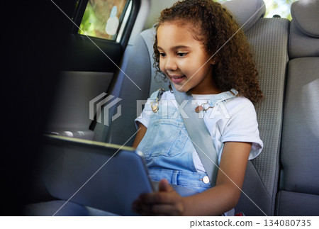 Child in car, tablet and video on road trip with seatbelt for safety and device to play educational online game. Technology, internet browsing and travel, happy girl on backseat for drive or carpool. 134080735