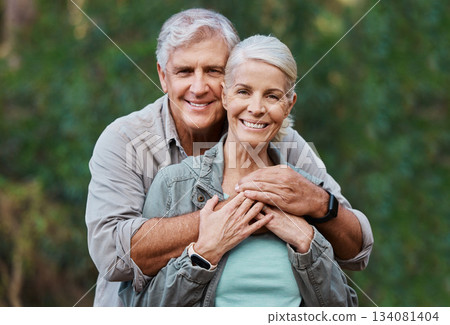 Love, portrait and elderly couple hug in a forest for hiking, relax and walking in nature on blurred background. Face, embrace and happy senior man with woman on retirement vacation in the woods 134081404