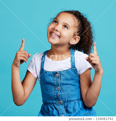 Happy, looking and a child pointing in a direction isolated on a blue background in a studio. Smile, thinking and a young girl showing up with a hand gesture, advertising and counting on a backdrop Happy, looking and a child pointing in a direction isolated on a blue background in a studio. Smile, thinking and a young girl showing up with a hand gesture, advertising and counting on a backdrop 134081742