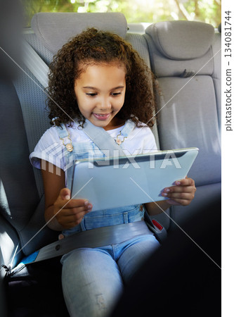 Happy, watching and a child in a car with a tablet for a movie, cartoons or video. Smile, travel and a girl sitting in a vehicle with tech, streaming online and enjoying a film for entertainment 134081744