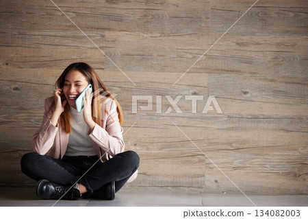 Woman, phone call and space for communication or connection in studio with advertising mockup. Happy female on wooden background laughing at funny conversation or listening and talking on smartphone 134082003