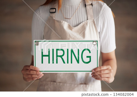 Woman, hands and hiring sign for small business recruitment, career or job opportunity against a studio background. Hand of female entrepreneur with apron holding billboard, label or poster for hire Woman, hands and hiring sign for small business recruitment, career or job opportunity against a studio background. Hand of female entrepreneur with apron holding billboard, label or poster for hire 134082004