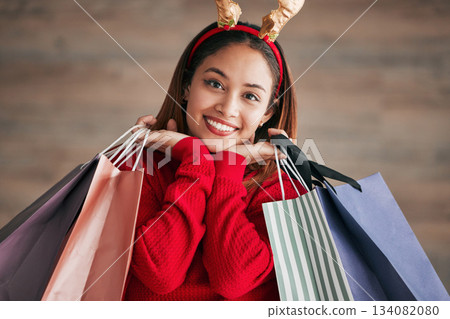 Portrait, christmas headband and female with shopping bags for a festive or holiday celebration. Happy, smile and face of a woman model with gifts or presents with xmas reindeer ears for an event. 134082080