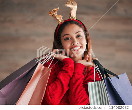 Shopping bags, portrait and woman with a christmas headband for a festive or holiday celebration. Happy, smile and face of a female model with gifts or presents with xmas reindeer ears for an event. Shopping bags, portrait and woman with a christmas headband for a festive or holiday celebration. Happy, smile and face of a female model with gifts or presents with xmas reindeer ears for an event. 134082082