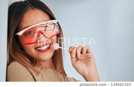 Lollipop, woman and smile with makeup, cosmetics and gen z style eating a sweet candy. Lips, young person and studio background with mockup and a female model with sweets and cool fashion sunglasses 134082103
