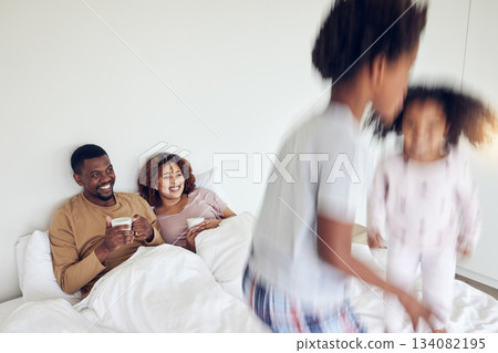 Mother, father and children jump on bed in morning for playing together, fun and quality time at home. Love, black family and happy mom and dad with motion blur kids with energy, jumping and excited 134082195