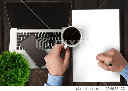 Man writing on paper while drinking coffee 134082422