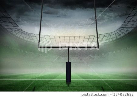 American football goal post is standing on green striped turf in misty stadium under overcast sky 134082682