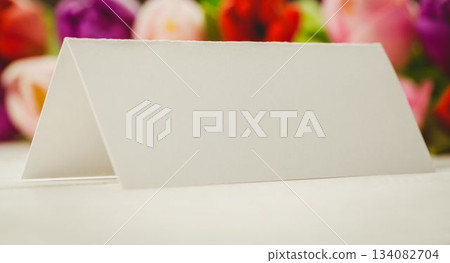 Showing blank white folded tent card resting on light tabletop, featuring multicolor tulip backdrop Showing blank white folded tent card resting on light tabletop, featuring multicolor tulip backdrop 134082704