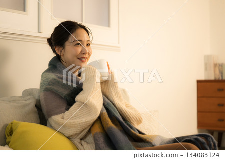 A young woman drinking a hot drink in a lit room at night. A winter image of a woman. A warm image of incandescent light. A young woman drinking a hot drink in a lit room at night. A winter image of a woman. A warm image of incandescent light. 134083124