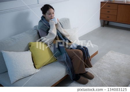 夜晚，一位年輕女子在燈光明亮的房間裡喝著熱飲。冬日裡的女性形象。俯瞰視角。 134083125