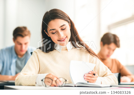 New Highschool Year On Campus. Positive Beautiful Young Adolescent Student Lady Sitting At Table In Modern Classroom, Doing Test Exercise, Reading Task, Enjoying Education And Learning New Highschool Year On Campus. Positive Beautiful Young Adolescent Student Lady Sitting At Table In Modern Classroom, Doing Test Exercise, Reading Task, Enjoying Education And Learning 134083326