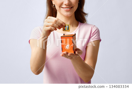 Garbage Sorting Conceptual Image With Lady Putting Card With Drawn Plastic Bottles Icon Into Small Wooden Toy Trash Container, Unrecognizable Lady Standing Over Light Background In Studio, Copy Space Garbage Sorting Conceptual Image With Lady Putting Card With Drawn Plastic Bottles Icon Into Small Wooden Toy Trash Container, Unrecognizable Lady Standing Over Light Background In Studio, Copy Space 134083334