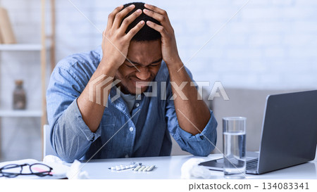 Black Man Suffering From Headache Touching Head Sitting At Workplace In Office. Unhappy African American Guy Having Migraine Feeling Bad During Work. Painful Severe Head Ache Concept. Black Man Suffering From Headache Touching Head Sitting At Workplace In Office. Unhappy African American Guy Having Migraine Feeling Bad During Work. Painful Severe Head Ache Concept. 134083341