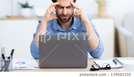 Unhappy Businessman Suffering From Headache Pain Touching And Massaging Aching Head Sitting At Laptop Computer In Modern Office. Health Problem, Painful Migraine Concept. Selective Focus 134083350