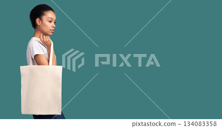 No Plastic. Black Girl Holding Blank White Eco Bag Posing Over Turquoise Studio Background. Panorama, Empty Space 134083358