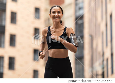 Healthy Lifestyle Concept. Sporty Young Arabic Female Jogging On Urban City Street, Athletic Woman In Stylish Sportwear And Phone Holder Armband Training Outdoors, Enjoying Running, Copy Space 134083368