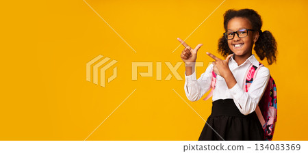Look. Smiling Black School Girl Pointing Fingers Aside Over Yellow Background In Studio. Panorama With Free Space For Text 134083369