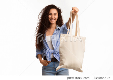 Use Eco Bag. Joyful Young Female Showing White Textile Shopper Handbag Smiling To Camera Standing In Studio Over White Background. Minimalism And Eco-Friendly Lifestyle 134083426