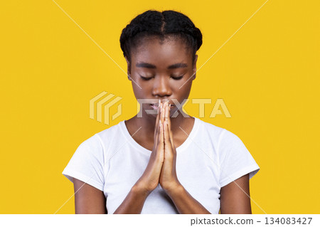 Peaceful African American Young Lady Praying Holding Clasped Hands In Prayer Gesture Standing With Eyes Closed Posing In Studio Over Yellow Background. Portrait Of Black Woman Sending Prayers To God 134083427
