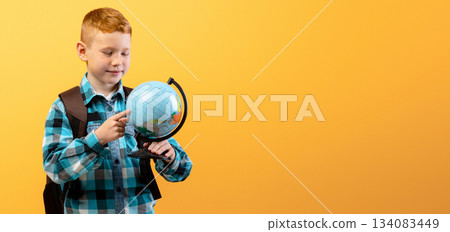 Positive schoolboy with backpack holding globe, studying geography on yellow studio background, copy space. Happy boy going to school, enjoying his school days. Kids education concept Positive schoolboy with backpack holding globe, studying geography on yellow studio background, copy space. Happy boy going to school, enjoying his school days. Kids education concept 134083449