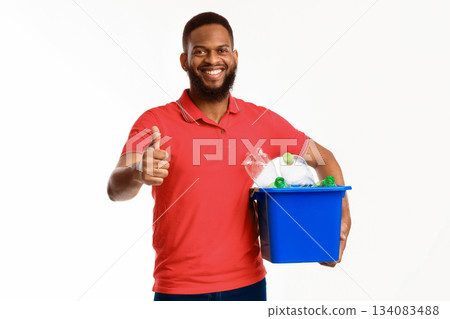 Happy Black Guy Showing Like Gesture Holding Bucket With Recycle Symbol And Wasted Plastic Litter Standing On White Studio Background. Male Approving Waste Sorting Concept 134083488
