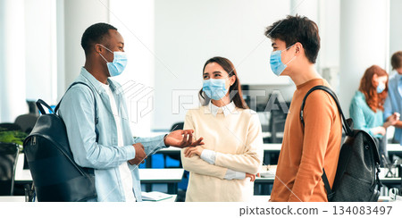 Healthcare, Education, Lifestyle And People Concept. Group of smiling diverse international students wearing protective medical masks and talking, standing in lecture hall at the university 134083497