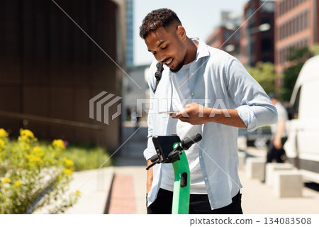Electric push scooter sharing services. Young black guy renting motorized kick e-scooters in the city, paying online with smartphone. Urban lifestyle 134083508