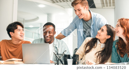 Positive Social Interaction. Cheerful international friends enjoying cooperation and collaboration, using pc laptop and talking, sharing ideas preparing group project in college library together 134083520