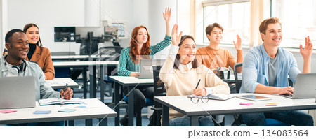 Smiling multicultural people raising hands to agree or to ask questions at modern seminar in office, diverse mixed race group of men and women sitting at desk with laptop computer listening to speaker Smiling multicultural people raising hands to agree or to ask questions at modern seminar in office, diverse mixed race group of men and women sitting at desk with laptop computer listening to speaker 134083564
