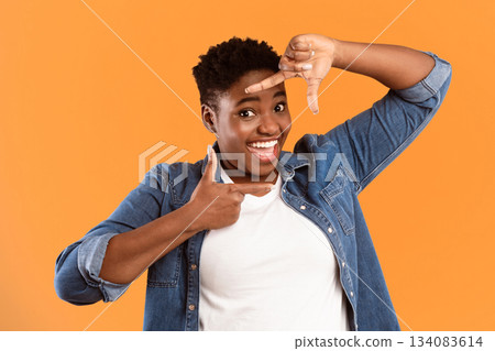 Capture The Moment. Smiling Black Plus-Size Lady Framing Face With Fingers Posing Looking At Camera On Yellow Background. Studio Shot. Frame Your Beauty Concept. Capture The Moment. Smiling Black Plus-Size Lady Framing Face With Fingers Posing Looking At Camera On Yellow Background. Studio Shot. Frame Your Beauty Concept. 134083614