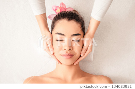 Young asian woman enjoying skin lifting face massage, getting professional beauty treatments at wellness center, attractive female relaxing on massage table with closed eyes, top view with copy space Young asian woman enjoying skin lifting face massage, getting professional beauty treatments at wellness center, attractive female relaxing on massage table with closed eyes, top view with copy space 134083951