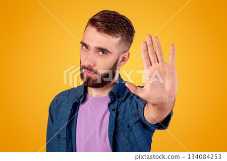 Serious hipster guy gesturing STOP, showing palm to camera over grey studio background. Young man expressing his negative attitude, rejecting or prohibiting something 134084253